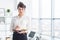 Beautiful businesswoman standing in office, holding notebook, planning meetings for the work day, looking at camera.