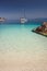 Beautiful calm azure blue lagoon with sailing catamaran yacht boat at anchor. Pure white pebble beach with rocks in the