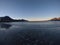 Beautiful calm blue waves hitting white frozen sandy beach in late autumn in the arctic circle with deep mountain and open sea