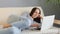 Beautiful calm relaxed woman wearing striped shirt and jeans laying down on cozy couch and using laptop for online communication,