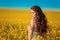 Beautiful carefree girl with long curly healthy hair over Yellow rape field landscape background. Attracive brunette with blowing