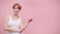 Beautiful casualy dressed middle aged redhead woman pointing finger on empty space isolated on pink background