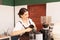 Beautiful caucasian barista woman standing and scooping coffee beans from coffee equipment into coffee bean grinder in cafe coffee
