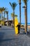 Beautiful Caucasian Blond Girl With Back Leaning On Her Yellow Board Waiting On The Promenade Her Surf Class On The Beach Of The