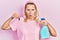 Beautiful caucasian blonde woman holding cockroach and pesticide sprayer making fish face with mouth and squinting eyes, crazy and