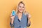 Beautiful caucasian blonde woman holding glucometer device screaming proud, celebrating victory and success very excited with
