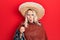 Beautiful caucasian blonde woman wearing festive mexican poncho drinking tequila shot scared and amazed with open mouth for