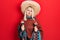 Beautiful caucasian blonde woman wearing festive mexican poncho and maracas relaxed with serious expression on face