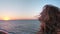 Beautiful caucasian curly blond young woman at sunrise or sunset by the ocean. The wind develops the hair. She breathes