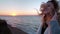 Beautiful caucasian curly blond young woman at sunrise or sunset by the ocean. The wind develops the hair. The concept