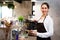 Beautiful Caucasian female barista using tablet and smiling inside coffee shop