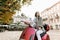 Beautiful Caucasian girl with long dark hair is smiling while riding red scooter and looking at beautiful ancient city