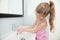 Beautiful caucasian little girl with long hair washing hands with fresh water in bathroom
