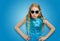 Beautiful Caucasian little girl in sunglasses and blue dress looks angrily into the camera. Emotions and adolescent