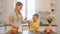 Beautiful caucasian Mom with long white hair pouring out a glass of milk for her cute son in yellow shirt. Modern