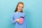 Beautiful caucasian teenager girl with brown hair in blue hoody drinks coffee with pink cup  on blue background