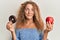 Beautiful caucasian teenager girl holding red apple and donut smiling looking to the side and staring away thinking