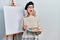 Beautiful caucasian woman drawing with palette on easel stand angry and mad screaming frustrated and furious, shouting with anger