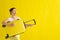 Beautiful caucasian woman fooling around with a suitcase on a yellow background.