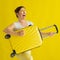 Beautiful caucasian woman fooling around with a suitcase on a yellow background. A charming girl imitates playing the