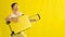 Beautiful caucasian woman fooling around with a suitcase on a yellow background. A charming girl imitates playing the