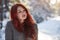 Beautiful charming girl with red hair in the winter park. Pensive, dreamy, loving look. Cold weather.