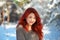 Beautiful charming girl with red hair in the winter park. Pensive, dreamy, loving look. Cold weather. Trees in the snow