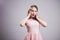 A beautiful charming young woman wears a pink dress and standing near the gray background is surprised, grabs her head with her ha