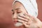 Beautiful cheerful Asian teen girl applying facial clay mask. Beauty treatments, isolated on light background