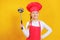 Beautiful chef little girl holding a soup ladle in her hands. A child in uniform on a yellow background