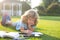 Beautiful child boy with book writing notes in copybook on grass background. Kids reading book in park.