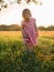 Beautiful child girl in grass with sunset tones. Cute baby in pink dress in park