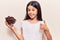 Beautiful child girl holding chocolate cereals smiling happy and positive, thumb up doing excellent and approval sign