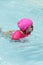 Beautiful child learning to swim in the pool with a pink float.