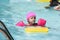 Beautiful child learning to swim in the pool with a pink float.