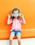 Beautiful child listens to music in headphones over colorful orange background