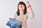 Beautiful Chinese shopkeeper woman holding folded jeans over isolated white background annoyed and frustrated shouting with anger,