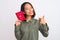 Beautiful chinese woman holding Japan Japanese passport over isolated white background happy with big smile doing ok sign, thumb