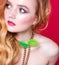 A beautiful choker made of gold chains and green fluff around the neck of a red-haired girl. Woman posing on red