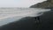 Beautiful cinematic shot. A young couple runs by the arm along a black volcanic sand beach. Aerial view of Tenerife