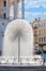 A beautiful city fountain in the form of a huge dandelion refreshes people against the background of the arched-column facade of