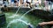 A beautiful city fountain in a large park against the backdrop of many people walking and relaxing. Cool water in the city