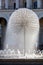 A beautiful city fountain in the shape of a huge dandelion refreshes passers-by against the background of the arched-column facade
