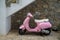 Beautiful classic design pink color Vespa scooter with white seat cushion parking on gravel wash sidewalk under stair