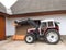 A beautiful clean tractor stands near a tiled roof shed