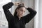 Beautiful closeup of a girl banding her ponytail in a black shirt against a blurry background