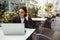 Beautiful concentrated freelance woman, young business person, copywriter, using laptop while sitting at table in a terrace of