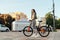 Beautiful concentrated hispanic female in an urban scenery in stylish sportswear is holding her orange bike and looking far ahead