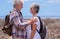 Beautiful couple of senior travelers with backpack looking in the eyes in outdoors excursion.  Horizon over sea