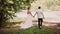 Beautiful couple share wedding day. They walk in park near river holding hands. Bride and handsome groom. Steadicam shot